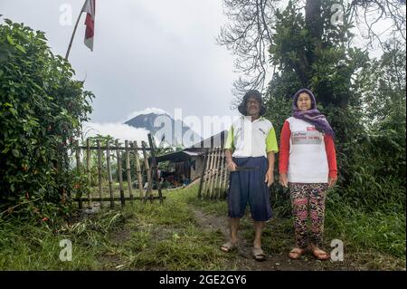 Una coppia sposata del popolo indigeno Karonese, H Alamsyah Pinem, 69, visto in ritratto insieme a sua moglie, Sarinan Br Sitepu, 64, in piedi a casa loro con il vulcano Sinabung essere uno sfondo nel villaggio di Sibintun, Simpang Empat, Karo, Sumatra Nord, Indonesia il 16 agosto 2021. L'innalzamento della bandiera indonesiana commemora il 76° anniversario dell'indipendenza dell'Indonesia. Foto di Sutanta Aditya/ABACAPRESS.COM Foto Stock