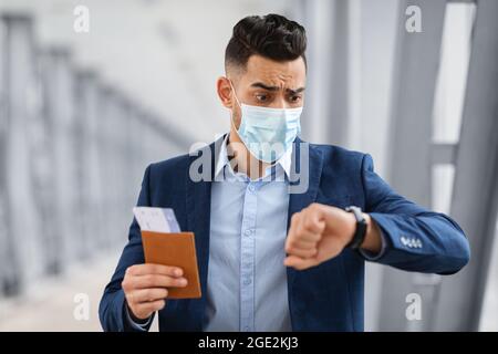 Uomo arabo preoccupato in maschera guardando il orologio da polso, arrivare tardi per il volo Foto Stock