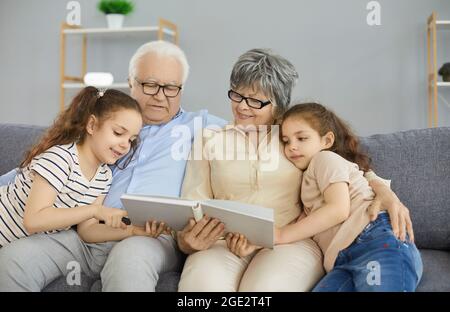 Buona nonna, nonno e nipoti che leggono un libro o guardano attraverso un album fotografico di famiglia Foto Stock