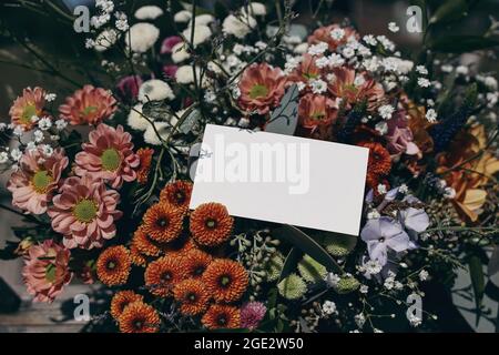 Moody femminile matrimonio, compleanno mockup scena. Primo piano di carta bianca, etichetta regalo su bouquet floreale colorato alla luce del sole. Gypsofila e. Foto Stock