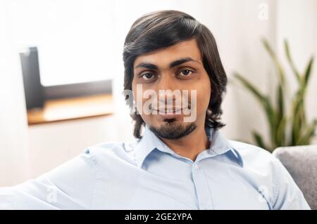 Primo piano ritratto di bel giovane indiano misto-razza in camicia casual. Un ragazzo orientale dai capelli scuri bearded guarda la telecamera con un sorriso amichevole Foto Stock