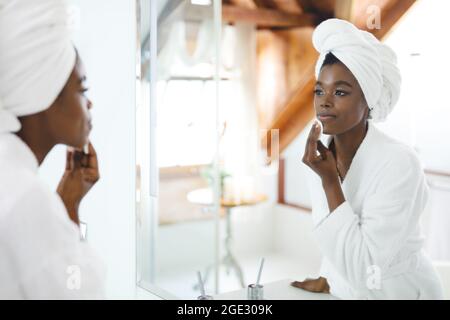 Donna afroamericana sorridente in bagno, viso detergente con tampone di cotone per la cura della pelle Foto Stock