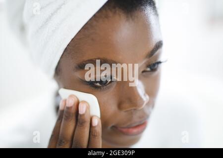 Donna afroamericana sorridente in bagno che pulisce il suo viso con un tampone di cotone per la cura della pelle Foto Stock