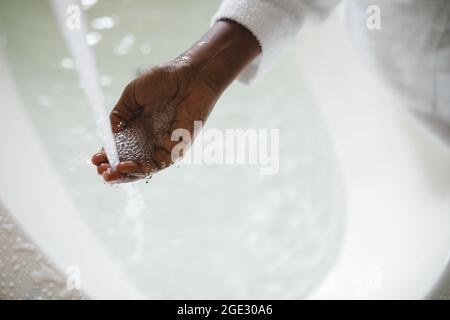 Primo piano di mano di donna afroamericana in bagno che fa funzionare un bagno Foto Stock