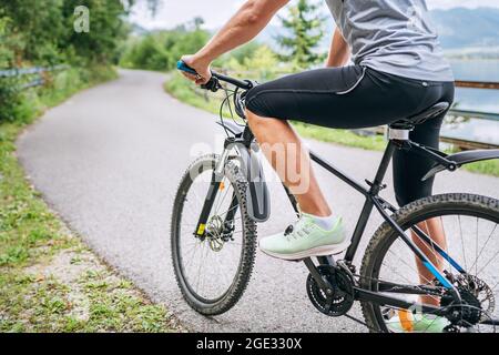 Foto ravvicinata di un uomo vestito da ciclismo che inizia a guidare una bicicletta moderna sulla pista ciclabile asfaltata fuori città. Persone sportive attive conc Foto Stock