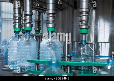 Bottiglie di plastica da 5 litri in fase di riempimento con acqua in una macchina di riempimento. Produzione alimentare Foto Stock