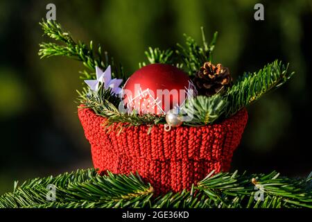 Un cesto rosso a crocheted con rami di abete e una palla rossa di albero di Natale su sfondo verde Foto Stock
