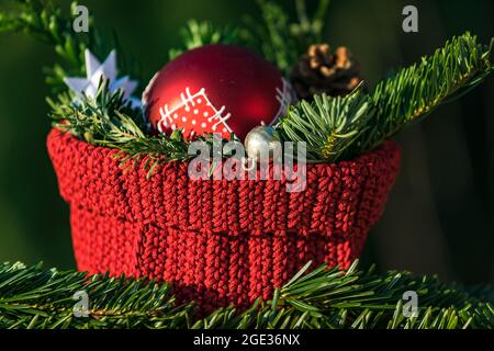 Primo piano di una decorazione natalizia con rami rossi di bauble e abeti davanti a uno sfondo naturalmente verde Foto Stock