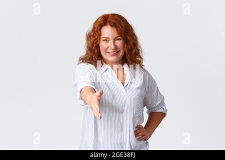 Fiducioso sorridente metà-età redhead imprenditore femminile, donna d'affari estendere la mano per handshake, salutare partner commerciale, presentarsi come Foto Stock