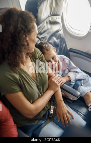 Vista ad alto angolo della bambina seduta sull'aereo, appoggiata sulla madre mentre viaggia insieme Foto Stock