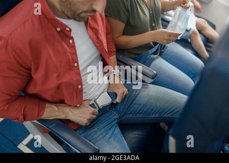 Vista ad alto angolo della cintura di sicurezza di fissaggio del passeggero maschio mentre si è seduti sull'aereo per un volo sicuro Foto Stock