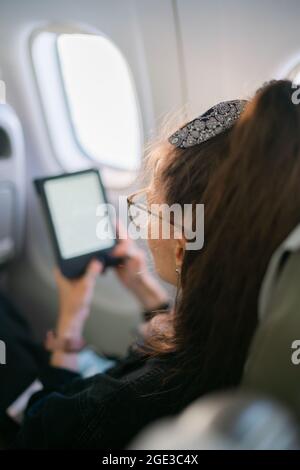 Donna brunetta che legge e-book durante il volo in aereo Foto Stock