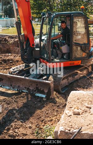 Lavoratore che guida un escavatore in un cantiere. Foto Stock