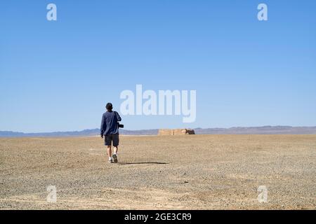 vista posteriore di un fotografo asiatico che cammina nel deserto di gobi sotto la telecamera con cielo blu Foto Stock