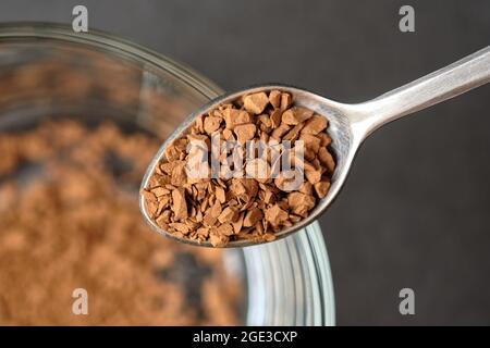 Congelare il caffè istantaneo essiccato su cucchiaino da tè con fondo tazza di caffè in vetro. Foto Stock