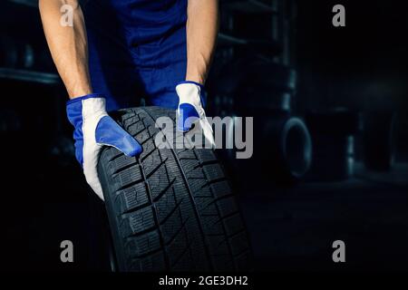 meccanico che tiene il pneumatico dell'auto su sfondo scuro dell'officina con spazio di copia. servizio pneumatici Foto Stock
