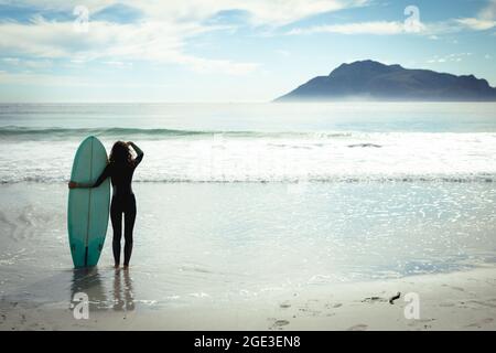 Razza mista donna che tiene surf in mare il giorno di sole Foto Stock