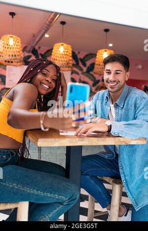 Amici multiculturali che prendono selfie su smartphone mentre si siedono insieme in un ristorante poke. Foto Stock
