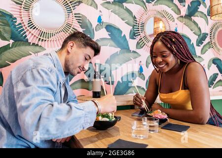 Amici multiculturali seduti in un ristorante e gustando una sana ciotola di poke. Foto Stock