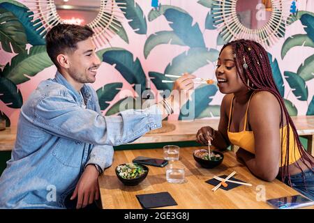 Amici multiculturali seduti in un ristorante e gustando una sana ciotola di poke. Foto Stock