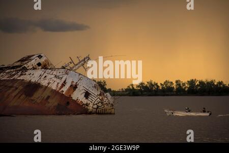 Grande nave sommersa nel fiume 'ataco' con una piccola barca che si insila accanto con un cielo arancione al tramonto Foto Stock