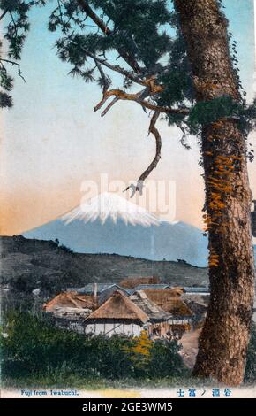 Vecchia cartolina giapponese colorata a mano, circa 1900, del Monte Fuji con il villaggio di Iwabuchi in primo piano incorniciato sul lato da un albero. Foto Stock