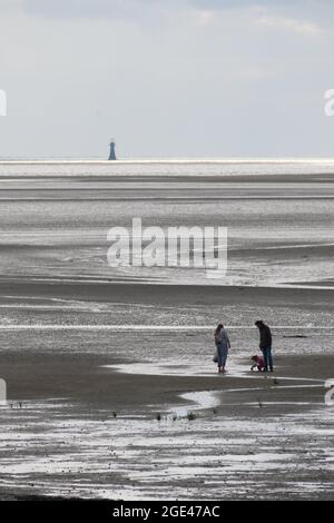 Llanelli, Carmarthenshire, Regno Unito. 16 agosto 2021. Regno Unito Meteo: Incantesimi soleggiati ma una brezza fresca alla spiaggia di Llanelli, Carmarthenshire. Una famiglia esplora le sabbie con la bassa marea mentre l'ultimo faro di Whitford domina l'orizzonte. Credit: Gareth Llewelyn/ Alamy Live News Foto Stock