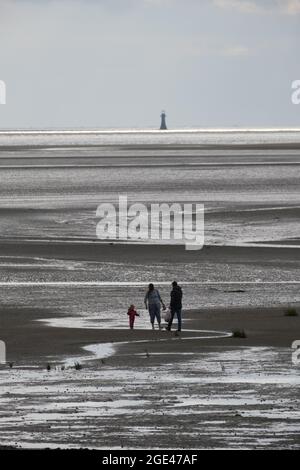 Llanelli, Carmarthenshire, Regno Unito. 16 agosto 2021. Regno Unito Meteo: Incantesimi soleggiati ma una brezza fresca alla spiaggia di Llanelli, Carmarthenshire. Una famiglia esplora le sabbie con la bassa marea mentre l'ultimo faro di Whitford domina l'orizzonte. Credit: Gareth Llewelyn/ Alamy Live News Foto Stock