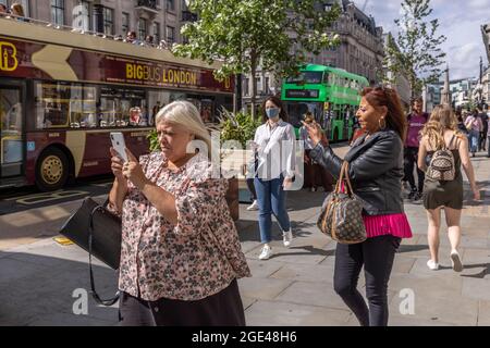 I turisti scattano fotografie sui loro smartphone mentre si trovano a Regent Street, nel centro di Londra, nel Regno Unito Foto Stock