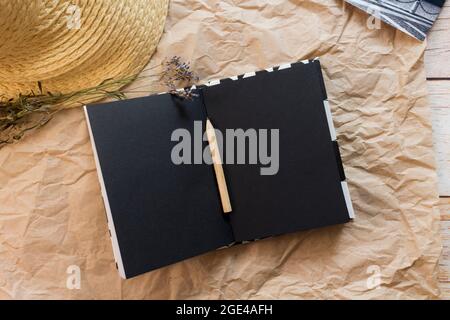 Composizione piatta con un taccuino nero vuoto aperto, matita, cartolina bianco-nero, lavanda secca e cappello di paglia su fondo di carta artigianale. Vista dall'alto. Foto Stock