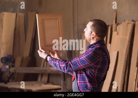 il falegname nei vestiti di lavoro guarda un proprio prodotto Foto Stock