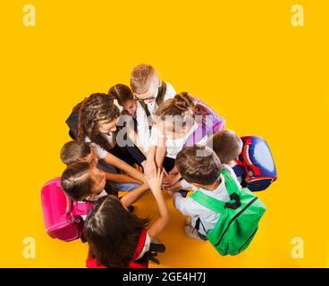 Gli scolari stanno accatastando le mani insieme sullo sfondo giallo Foto Stock