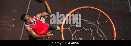 Vista dall'alto di un uomo afro-americano eccitato che gioca a basket vicino al cerchio, banner Foto Stock