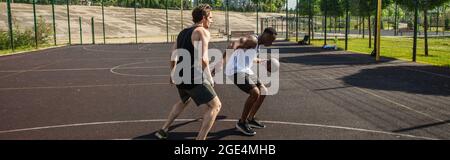 Vista laterale dell'uomo afro-americano che gioca a basket con un amico sul parco giochi all'aperto, banner Foto Stock