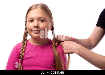 La madre sta facendo di trecce su piccola figlia alla testa. Parrucchiere è un intreccio di capelli su una giovane ragazza. Ottenere pronto per la scuola. Foto Stock