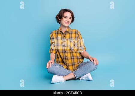 Foto di adorabile signora tranquilla seduta pavimento toothy beaming sorriso indossare camicia a scacchi isolato colore blu sfondo Foto Stock