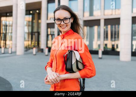 Giovane donna con bicchieri che tengono una borsa che cammina in città. Foto Stock