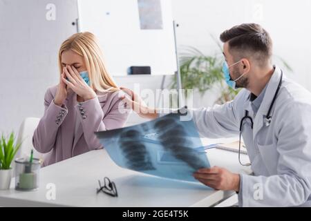 medico con i polmoni x-ray calmante sconvolto donna piangendo in maschera medica Foto Stock