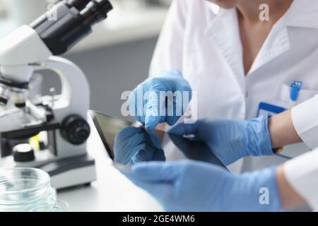 Gli scienziati in guanti sterili tengono la compressa nel guardaroba del laboratorio Foto Stock