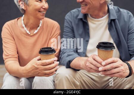Primo piano di una coppia matura felice che gusta il caffè all'aperto in città, con un'attenzione particolare alle tazze di carta in mano Foto Stock