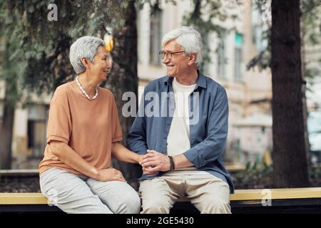 Ritratto di coppia anziana moderna che si guarda l'un l'altro mentre si siede sulla panchina nel parco e godendo di data romantica, spazio copia Foto Stock