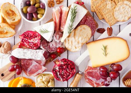 Salumi a bordo di formaggi assortiti, carni e antipasti. Tavola con vista dall'alto su sfondo di legno bianco. Foto Stock