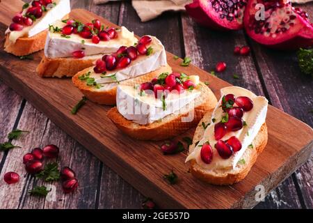 Antipasti di crostini con brie, melograni e prezzemolo. Primo piano su una tavola da servizio su uno sfondo rustico di legno. Festa cibo conce Foto Stock