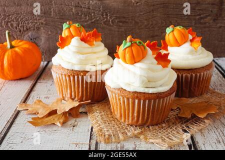 Fall zucca spezie cupcakes con crema glassa e guarnizioni autunnali. Primo piano su uno sfondo rustico di legno. Foto Stock