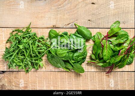 Mescolare i fogli di insalata, l'Arugula, lo Spinach e il swiis Chard. Sfondo di legno. Vista dall'alto Foto Stock
