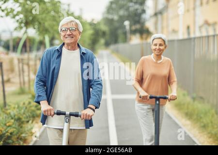 Vista frontale ritratto di una coppia moderna che cavalca gli scooter elettrici all'aperto in un bellissimo ambiente cittadino Foto Stock