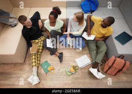 Vista dall'alto in un gruppo diverso di giovani studenti che studiano insieme mentre si siedono al piano della biblioteca dell'università Foto Stock