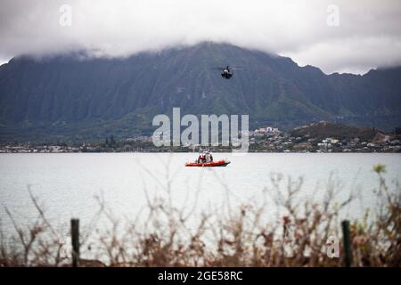 Il personale militare degli Stati Uniti con la base del corpo dei Marine Hawaii Provost, l'ufficio del Marshal e Waterfront Operations, postano la sicurezza su un'imbarcazione marina, mentre un Super Stallion CH-53 attaccato allo Squadron 463 dell'elicottero pesante della Marina vola in testa durante il letale Breeze 2021, MCBH, 10 agosto 2021. Lethal Breeze è un esercizio che dimostra la capacità della base di rispondere, comunicare e coordinare efficacemente le operazioni in più posizioni durante un incidente dinamico. (STATI UNITI Marine Corps foto di Lance CPL. Brandon Aultman) Foto Stock