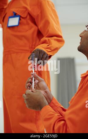 Riparatore che fa passare il cacciavite al collega che sta installando la lampada sul soffitto Foto Stock