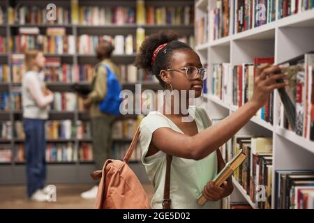 Vita ritratto di una studentessa africana-americana che sceglie libri nella biblioteca del college, copia spazio Foto Stock